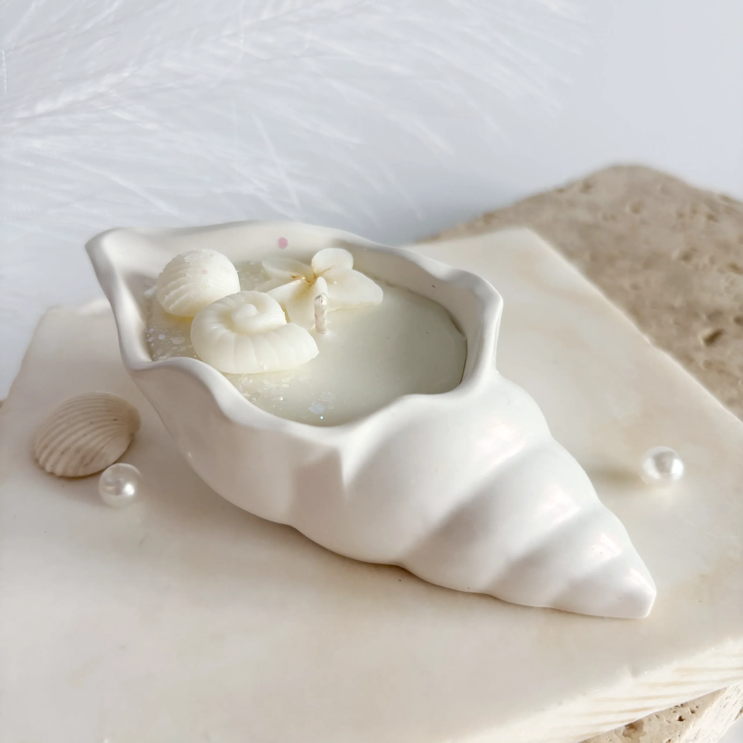 Vedere de profil a lumânării Perlina în formă de scoică ceramică sidefată, așezată pe un suport de marmură